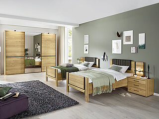 Sorrent: In Eiche teilmassiv/Absetzung Schiefer-Nachbildung, Schwebetürenschrank 3-türig (821), Außentüren massiv, Mitteltür Parsolspiegel, Griff- und Querriegel-Leisten in Schiefer-Nachbildung, ca. B 300, H 217, T 67 cm, 2x Komfort-Einzelbett (261)mit Holzkopfteil (getrennt), mit Stollenfußteil, ca. 100 x 200 cm, 2er-Set Konsolen (068), 3 Schubkästen, Front massiv, ca. B 60, H 48, T 43 cm. Gegen Aufpreis: Beleuchtung, Seitenstollen in Eiche massiv, Winkelpolster in Kunstleder anthrazit, 2er-Set Konsolenpaneel