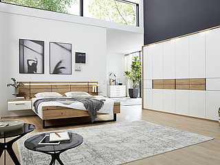 Suggestion 661 in white lacquer / contrasts in beamed oak veneer, 6-door hinge-door wardrobe, doors 2-5 with veneer truss and 3 raised strips in anthracite, doors 1-6 with 2 raised strips in anthracite, approx. W 300, H 229, D 60 cm, double bed with wooden headboard with raised strips in anthracite, footboard with runner in anthracite, 180 x 200 cm, BSH 48.6 cm, 2 wall-mounted nightstands, each with 1 drawer, cover panel in veneer, approx. W 60, H 25.3, D 42.2 cm (plus accessories)