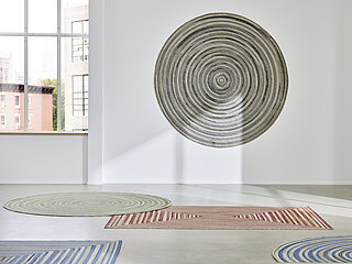 Outdoorteppich Solaro, 75 % Polypropylen, 25 % Polyester, Fb. 929 rot-beige und Fb. 634 beige-blau und 548 grün-beige, an der Wand: Fb. 335 grau-beige
