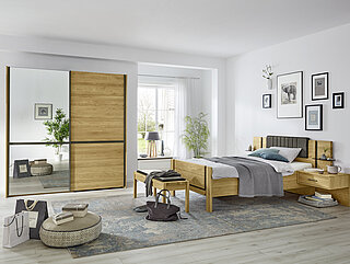 Sorrent: In Eiche teilmassiv/Absetzung Schiefer-Nachbildung: Schwebetürenschrank (818) mit Griff- und Querriegelleisten in Schiefer-Nachbildung, Tür links Parsol-Bronze-Spiegel, Tür rechts in Eiche massiv mit Kassetten-Optik, ca. B 200, H 217, T 67 cm, Komfortbett (305) mit Stollenfußteil, ca. 120/200 cm, 2 Konsolen (049) in schwebender Optik, 1 Schubkasten, ca. B 60, H 48, T 43 cm. Gegen Aufpreis: Seitenstollen, Polsterkopfteil in Kunstleder anthrazit, Aufsatzpaneel für Konsolen, Ankleidebank