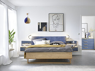 Malin: in Balkeneiche furniert, Absetzung Lack Lagune Blau, Doppelbett in Luxushöhe, ca. B 189, H 105, T 222 cm, Liegefläche ca. 180 x 200 cm, BSH 48,6 cm, Polsterkopfteil "Luna" in Stoff Maranta Lagune blau, 100 % Polyester, Fußteil mit Lisene, unten abgerundet und Kufe in Eiche, 2 Hängekonsolen mit je 1 Schubkasten, jeweils ca. B 60, H 23, T 46 cm. Zubehör: Paneelaufsatz links und rechts mit Holzboden (20216, 20226); indirekte LED-Holzbodenbeleuchtung (80027); 2er-Set LED-Flex-Leuchte Anthrazit, USB-Anschluss (80033). 