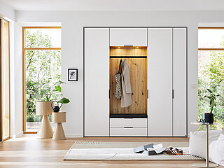 Garderobe des Modells Ovida in Farbe Eiche und Weiß der Marke Musterring
Vorzugskombination AVZ04, Korpus: Dekor Eiche Artisan, Front: Dekor Alpinweiß, Griffe und Haken in Schwarz, Sitzpolster in Anthrazit, ca. B 223, H 238, T 40 cm. Zubehör: 2 x LED-Unterbau-Spotbeleuchtung